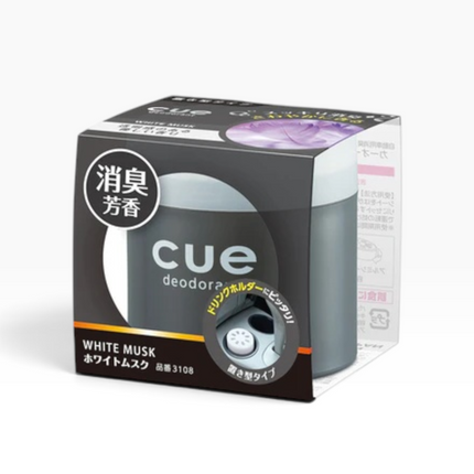 A box of cue deodorant in the White Musk scent, featuring a dark gray and black packaging design with white and orange text, and a clear window showing the gray cylindrical deodorant container inside.