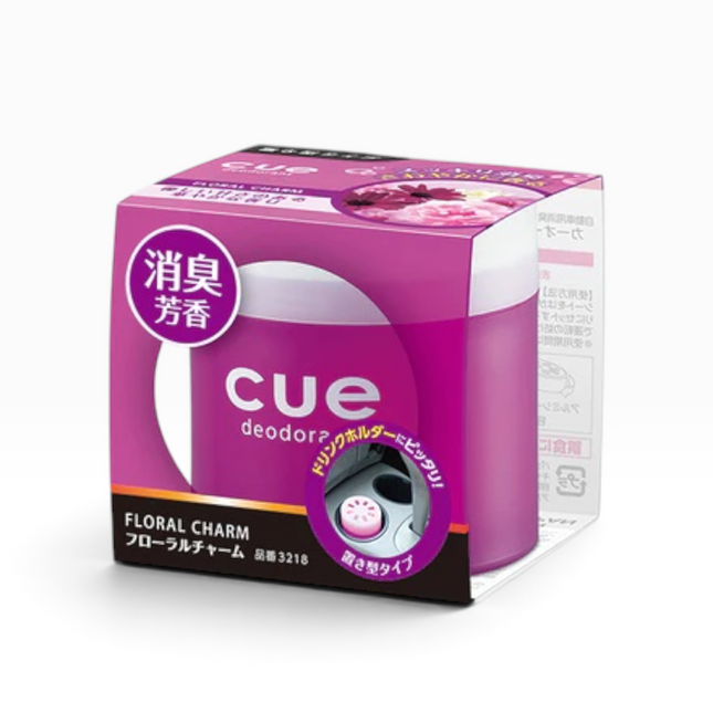 A box of Cue Deodorizer Floral Charm, featuring a pink and white design with a clear window showing the cylindrical deodorizer inside, set against a plain white background.