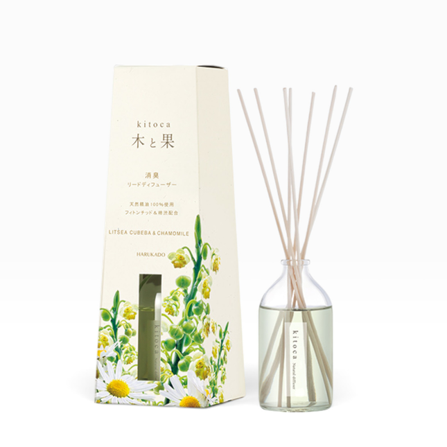 Kitoca reed diffuser set with a cream-colored box decorated with chamomile flowers, next to a clear glass bottle containing pale liquid and natural reed sticks, on a white background.