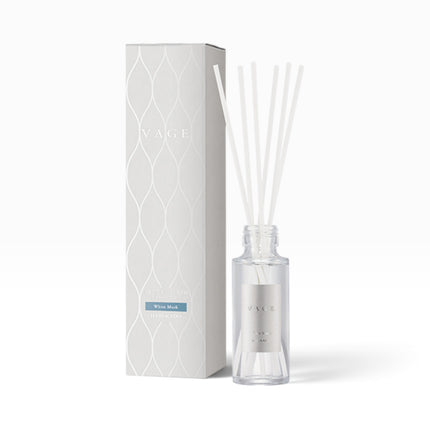 A VAGE reed diffuser bottle with clear glass and white reeds, standing next to its tall white packaging box with a subtle wavy pattern and a blue accent label.