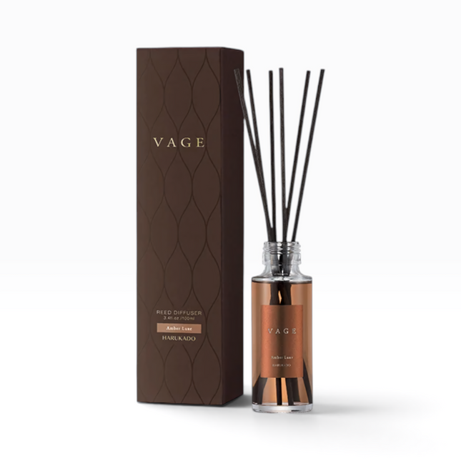 VAGE reed diffuser set featuring a dark brown textured box, a clear glass bottle filled with amber-colored liquid, and several black reeds, shown on a clean white background.