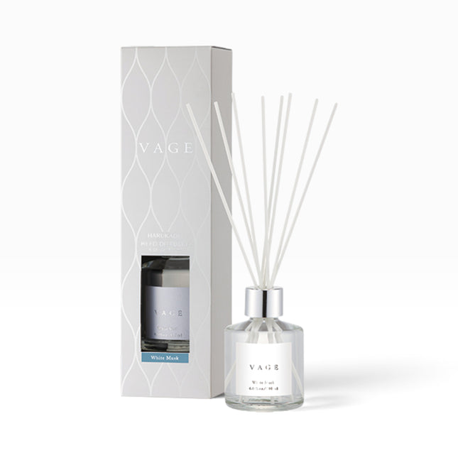VAGE reed diffuser with a clear glass bottle, white reeds, and a silver cap, standing next to its white patterned packaging box on a white background.