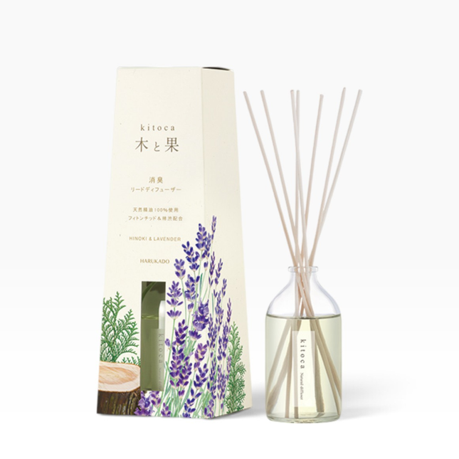 Kitoca reed diffuser set with a cream-colored box featuring lavender and green botanical illustrations, next to a clear glass bottle filled with pale liquid and natural reed sticks, on a clean white background.