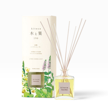 A reed diffuser bottle with pale yellow liquid and reeds stands in front of its illustrated cream-colored box. The box and bottle label read kitoca, with the scent name Littera Cudssa & Mint visible on the bottle.