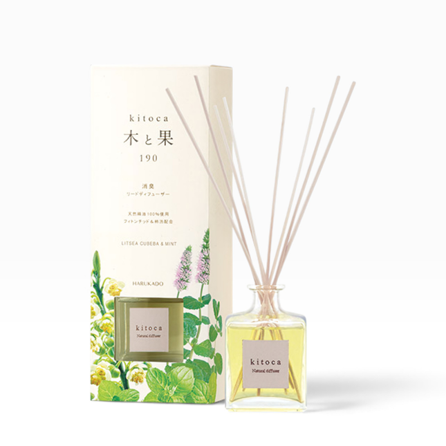 A reed diffuser bottle with pale yellow liquid and reeds stands in front of its illustrated cream-colored box. The box and bottle label read kitoca, with the scent name Littera Cudssa & Mint visible on the bottle.