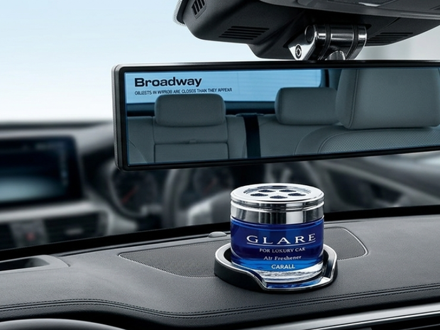 Car air freshener on a car dashboard with a rearview mirror displaying 'Broadway' in the background.