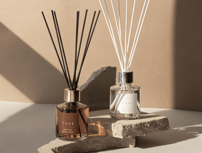 Two diffusers with sticks on a stone surface against a beige wall
